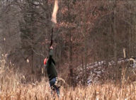 Photo of a hunter firing his rifle at a high-flying bird.